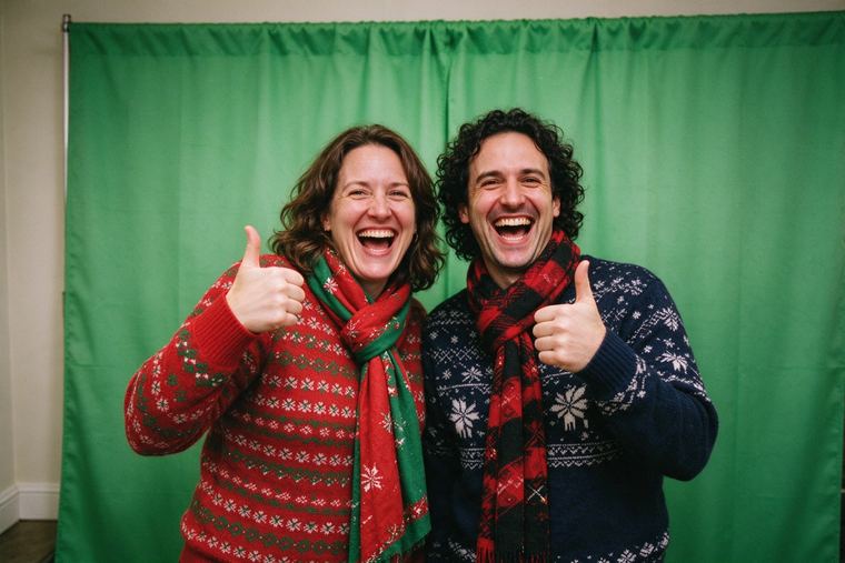Deux collègues en pull de Noël qui posent en riant devant un fond vert