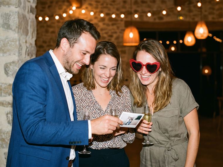 Collègues en tenue de soirée qui rient et lèvent leurs verres dans une salle de réception décorée, pendant une soirée d’entreprise