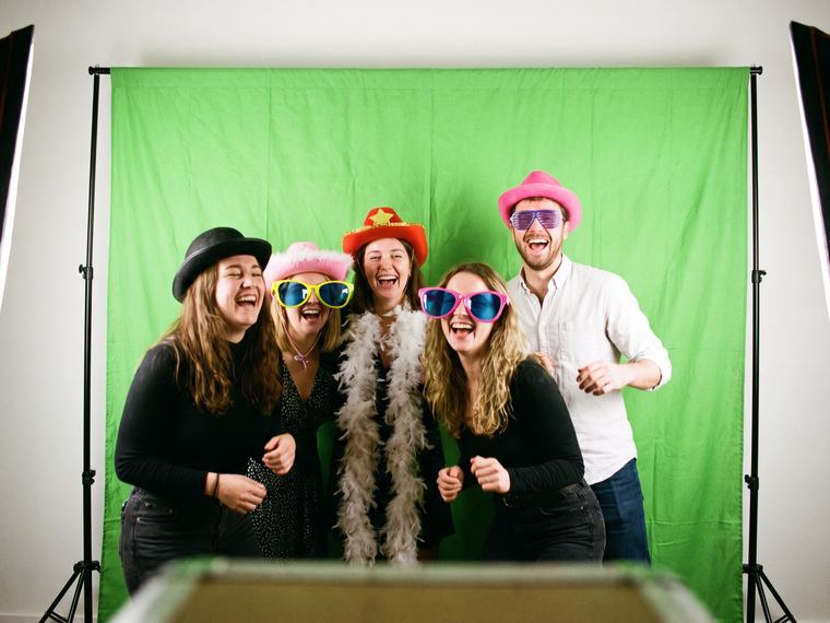 Groupe d’amis avec des accessoires de fête qui posent en riant devant un fond vert bien éclairé