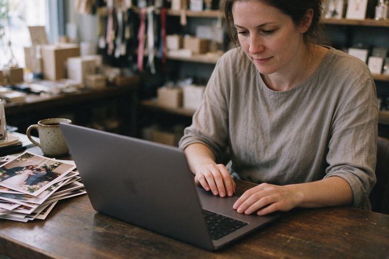 Commerçante concentrée sur son ordinateur portable dans l’arrière-boutique, une pile de tirages posée près du clavier
